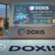İstanbul manzaralı modern bir ofis ortamında, Doxis logosu eşliğinde ISO 9001, ISO 27001 ve IDW PS 880 uyumluluk sertifikalarını gösteren dijital ekranlar ve belgeler.